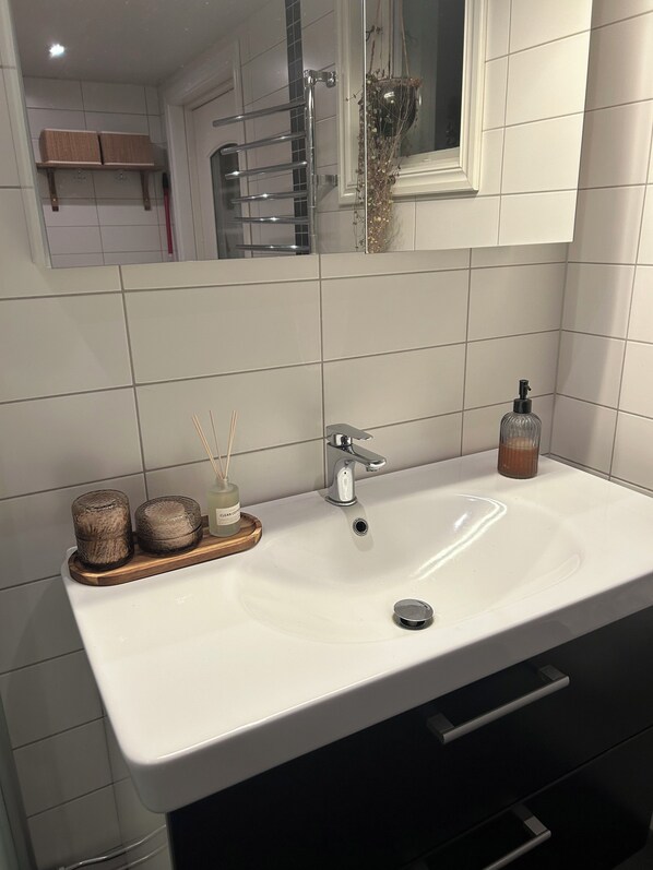 Un baño con lavamanos blanco, espejo, toallero y una botella de jabón para manos.