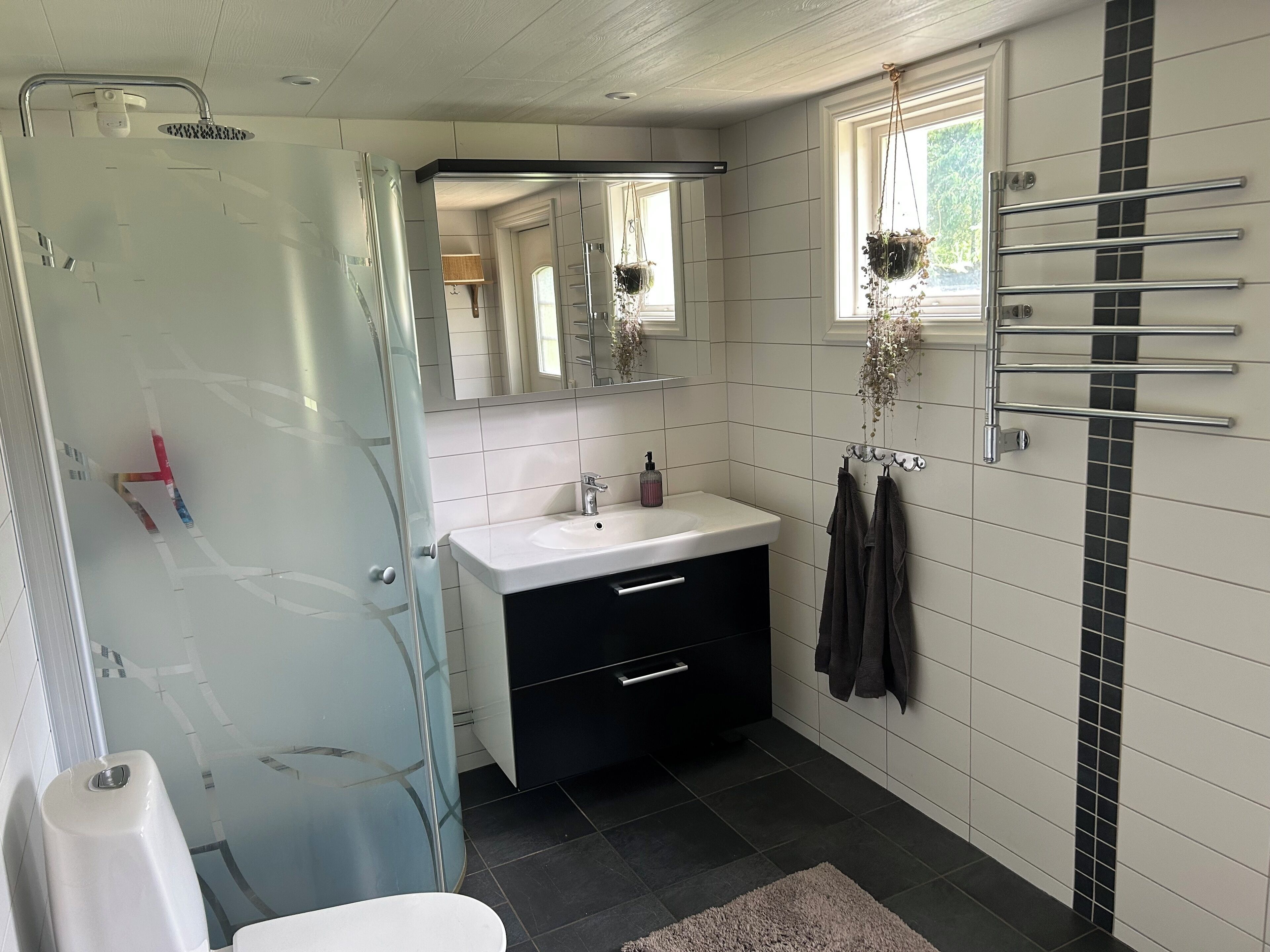 Une salle de bain avec une douche à parois de verre, un lavabo blanc, un meuble-lavabo noir et un porte-serviettes.