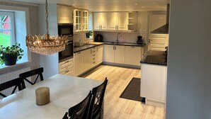 A modern kitchen with white cabinets, a chandelier, and a dining area with a table and chairs. - Large farmhouse near lake & forest • Boat included (Svängsta)