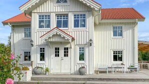 A white two-story house with a red-tiled roof, multiple windows, and a front porch with benches. - Large farmhouse near lake & forest • Boat included (Svängsta)