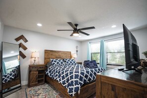 Ein Schlafzimmer mit Bett, Deckenventilator, Fernseher und Fenster mit Jalousien.