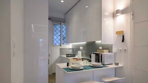 Cozinha moderna com armários brancos, uma ilha central com banquetas e uma janela com padrão geométrico.