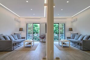 A modern living room with two sofas, a coffee table, and a chair. There are large windows and a balcony visible. - Icarus Minimal 2bedroom Bliss (Athina)
