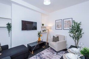 Ein modernes Wohnzimmer mit einer Couch, einem Couchtisch, einem Fernseher und einer Essecke für zwei Personen.