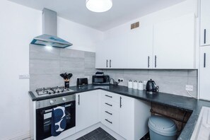 Een moderne keuken met een gasfornuis, oven, witte kastjes en een zwart aanrecht.