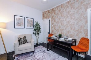 Een eetgedeelte met een tafel voor vier personen, een bank, een potplant en twee kunstwerken in lijsten aan de muur.