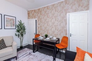 Een eetruimte met een tafel voor vier personen, twee stoelen, een potplant en een bank.