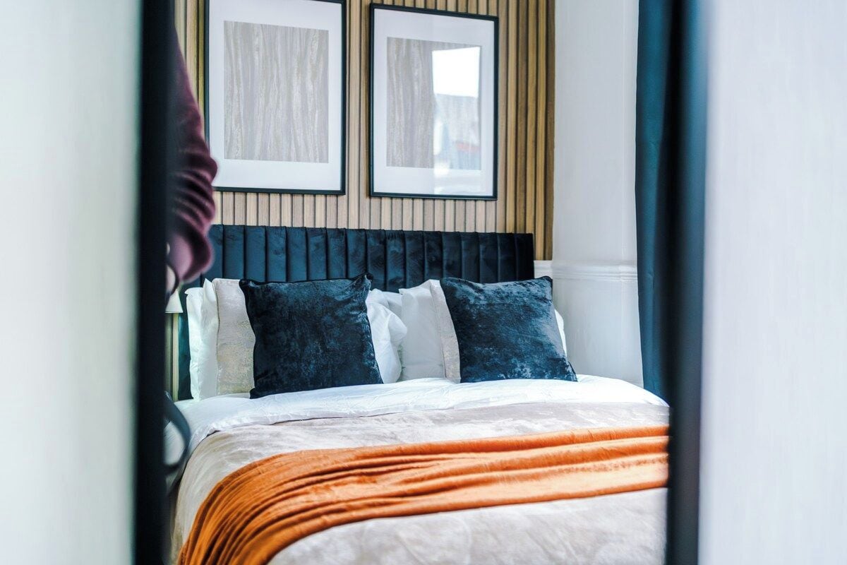 A bed with a dark headboard, white and blue pillows, and an orange blanket.