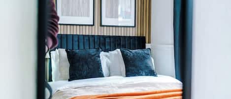 A bed with a dark headboard, white and blue pillows, and an orange blanket.