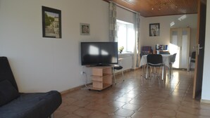 A living room with a sofa, a TV on a stand, a dining area with chairs and a table, and a kitchen area with cabinets. - Ferienwohnung fur Neun Personen in Homberg (Homberg)