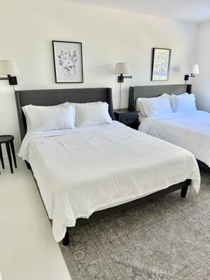 Ein Hotelzimmer mit zwei Betten, beide mit weißer Bettwäsche und einem grauen Kopfteil. An der Wand über jedem Bett befinden sich gerahmte botanische Drucke.