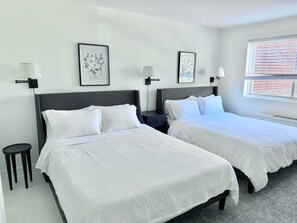 Habitación de hotel con dos camas, una mesita pequeña, lámparas fijadas a la pared e impresiones botánicas enmarcadas.