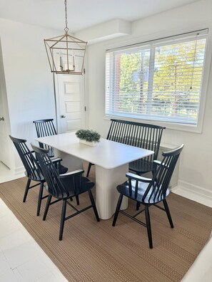A dining area with a white table, black chairs, a hanging light fixture, and a window with blinds. - Family Suite King Queen Queen + Queen sofa bed / Free Parking (Arlington)
