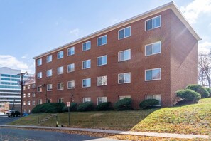 A multi-story brick building with a flat roof, rectangular windows, and a parking area with a scooter. - Family Suite King Queen Queen + Queen sofa bed / Free Parking (Arlington)