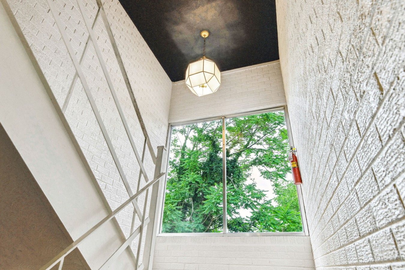 A room with a large window, white brick walls, and a hanging light fixture.