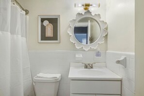 Un baño con lavamanos blanco, un espejo con marco decorativo, una toalla en el suelo y cortina de ducha.