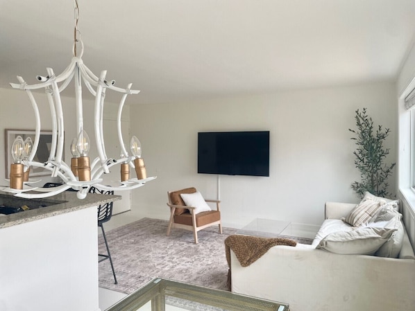 Un salon moderne avec un lustre, un téléviseur à écran plat, un canapé et un fauteuil.