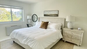 Un dormitorio con cama, mesita de noche, lámpara, espejo y ventana.