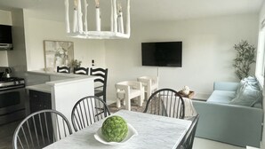 Una cocina moderna con armarios blancos, una mesa de comedor con sillas, un televisor de pantalla plana en la pared y un sofá azul claro en la sala.