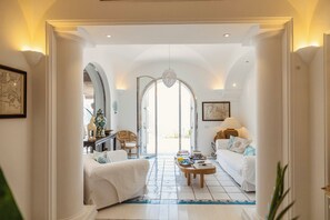 A spacious living area with a high ceiling, white walls, and a large arched doorway leading to a bright room. - Villa Monè by My Villa Collection (Capri)