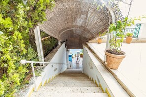 A staircase with a thatched roof structure, potted plants, and a view of an outdoor seating area. - Villa Monè by My Villa Collection (Capri)