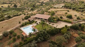 Vista aérea de una propiedad con piscina, patio y una casa grande rodeada de árboles y vegetación.