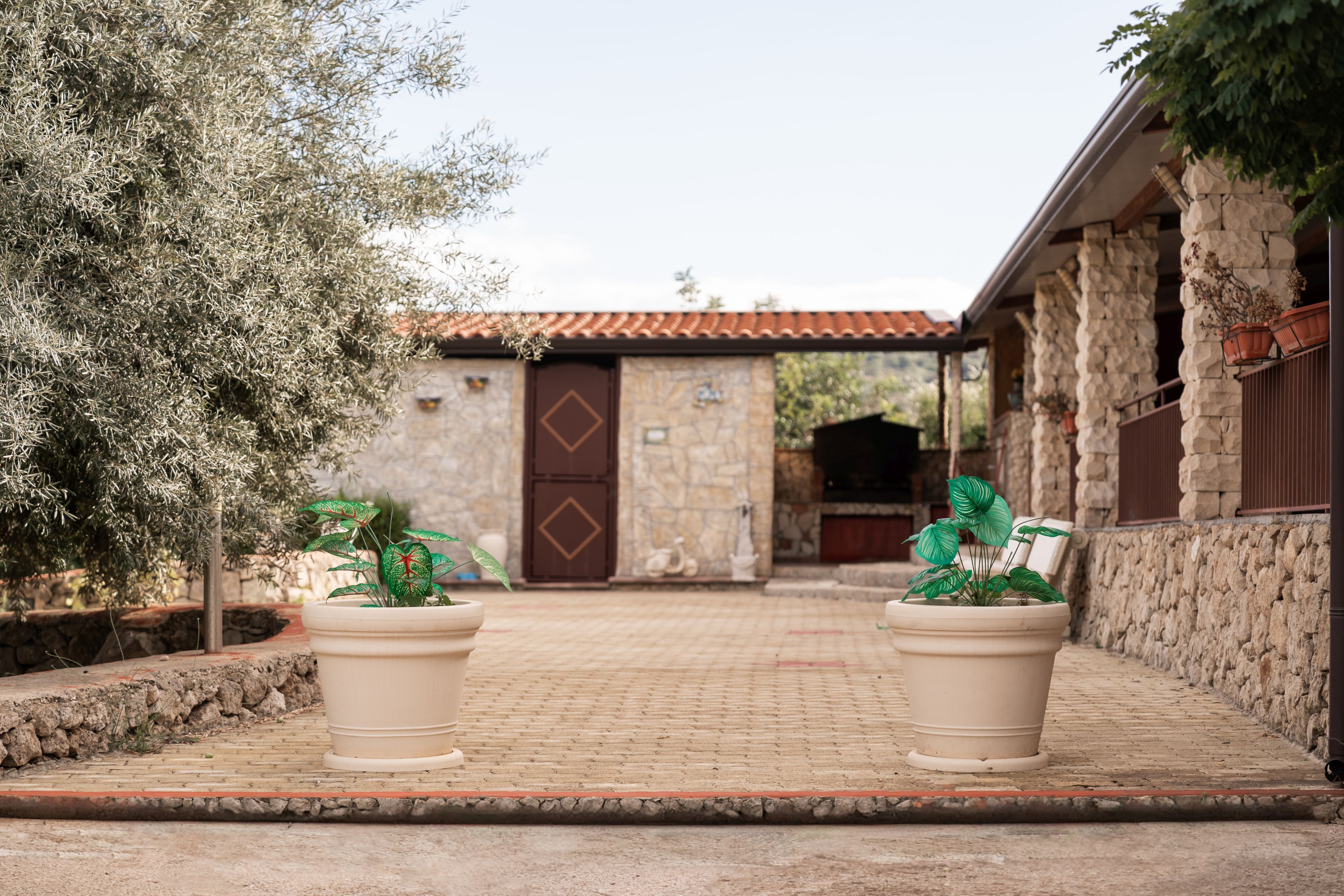 A stone building with a tiled roof, two potted plants, and a stone wall.