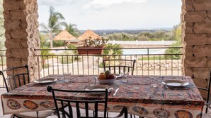 Una mesa dispuesta con platos, un cuenco de fruta y una copa, con vistas a un paisaje y una estructura de techo de paja.
