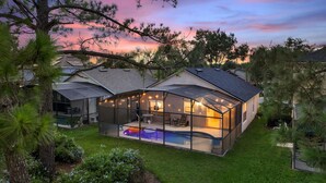 Ein Haus mit einer verglasten Terrasse, einem Swimmingpool und Blick auf den Himmel im Abendrot.