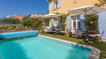 Une piscine avec une terrasse bleue, des meubles d’extérieur et des parasols.