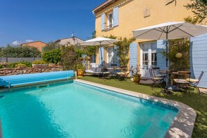 Ein Swimmingpool mit blauer Liegefläche, Gartenmöbeln und Sonnenschirmen.
