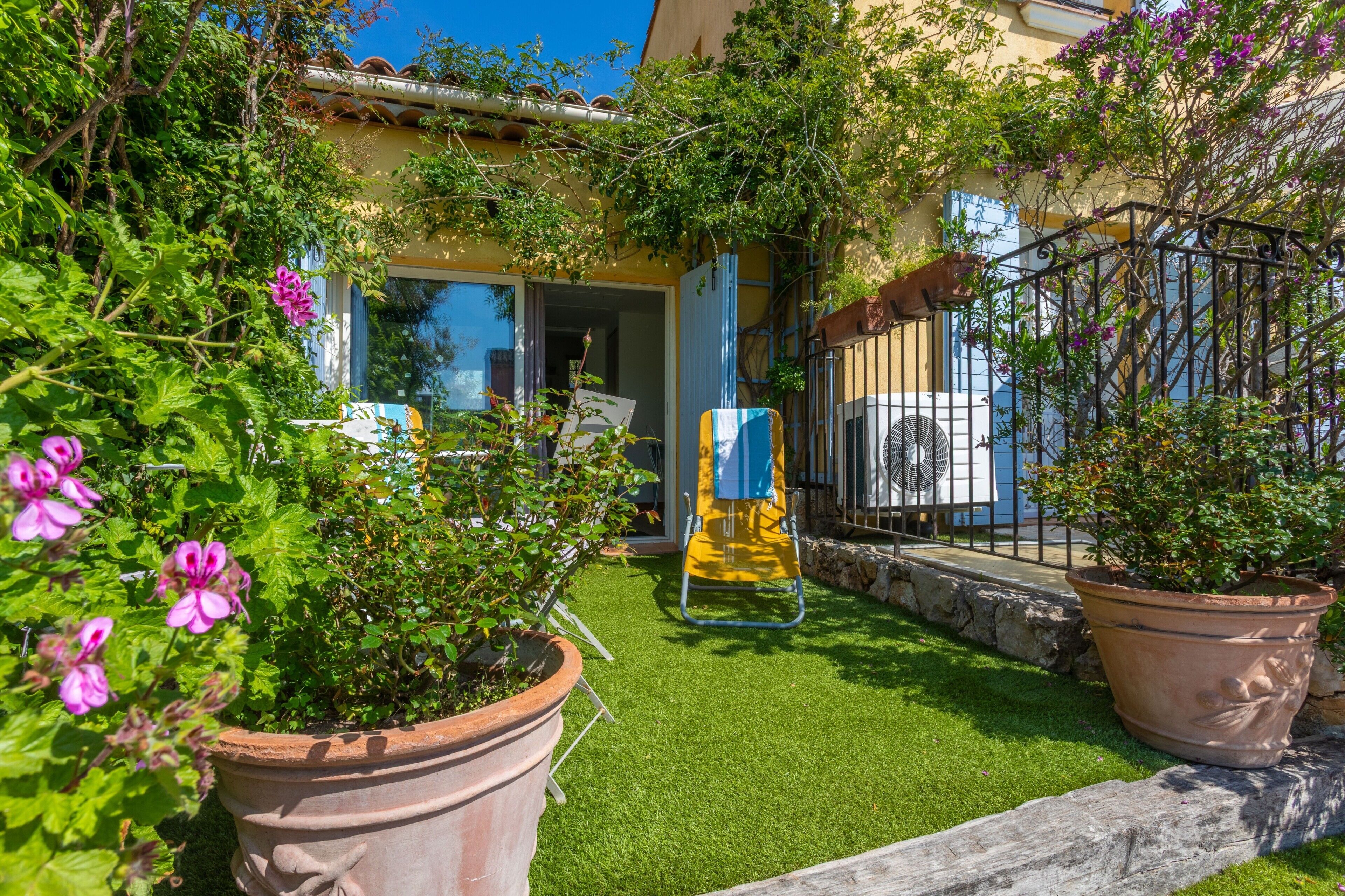 Une cour avec du gazon synthétique, des plantes en pot et une chaise jaune.