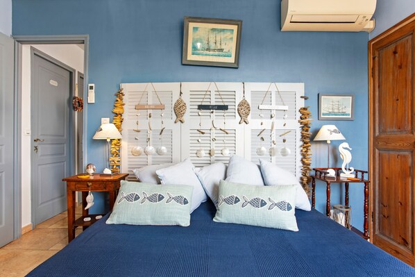 Une chambre avec une couvre-lit bleue, deux oreillers ornés de motifs de poissons, une tête de lit en bois agrémentée de décorations suspendues et un tableau encadré au-dessus du lit.