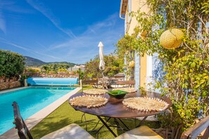 Zona junto a la piscina con mesa lista para comer, un banco azul y vista al estanque.