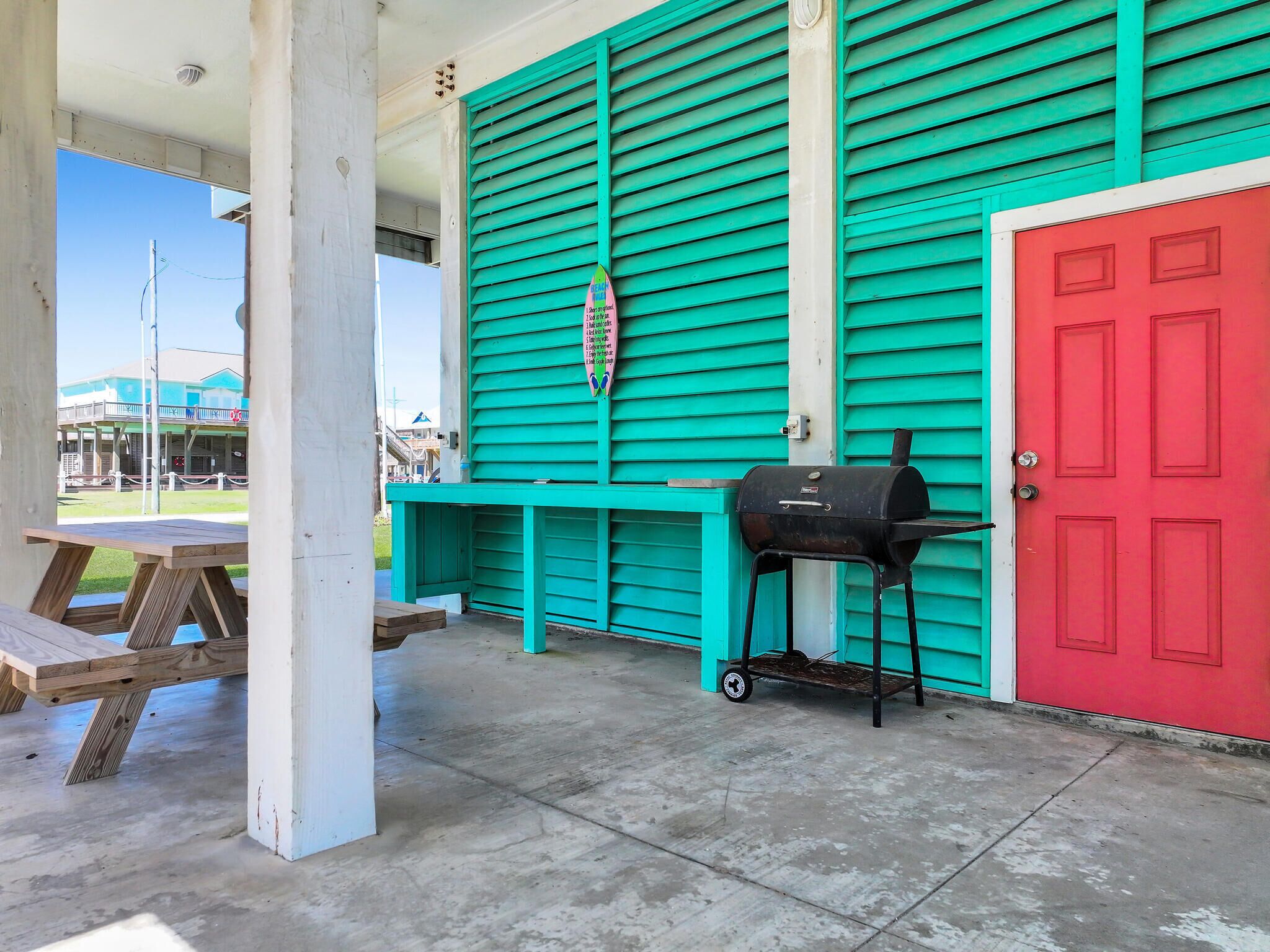 Un patio techado con una parrilla, una puerta roja y una pared color turquesa.