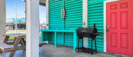 Un patio techado con una parrilla, una puerta roja y una pared color turquesa.