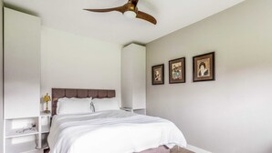 Ein Schlafzimmer mit einem Bett, einem Deckenventilator, einem Nachttisch und Wandbildern.