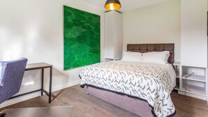 Ein Schlafzimmer mit Bett, Stuhl, Schreibtisch, einer grünen abstrakten Wand und einer Pendelleuchte.