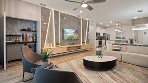 A modern living room with a flat-screen TV, a ceiling fan, and a dining area with a kitchen in the background. - NEW Mario World | Private Pool | Near Clubhouse (Davenport)
