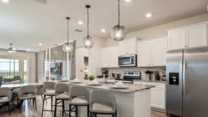 A modern kitchen with white cabinets, stainless steel appliances, and a bar area with stools. - NEW Mario World | Private Pool | Near Clubhouse (Davenport)