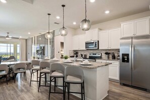 Una cocina moderna con armarios blancos, electrodomésticos de acero inoxidable y una zona de bar con taburetes.