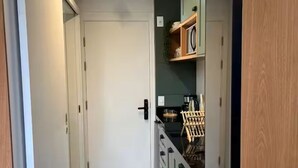 Un couloir étroit avec une porte au bout, un coin cuisine avec des placards et un comptoir, et un plancher en bois.