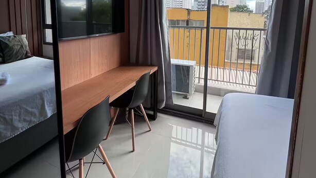Une chambre d’hôtel moderne équipée d’un lit, d’un bureau, d’une télévision et d’un balcon offrant une vue sur la ville.