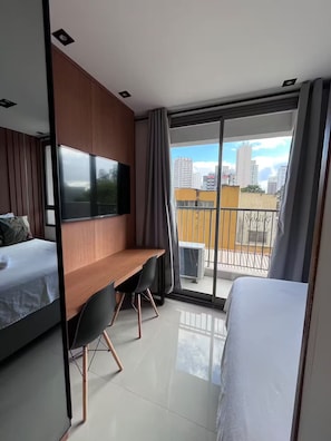 A modern hotel room with a bed, a desk, a TV, and a balcony with a city view. - Apartment in Santo Amaro, 7 minutes from the U.S. Consulate (São Paulo)