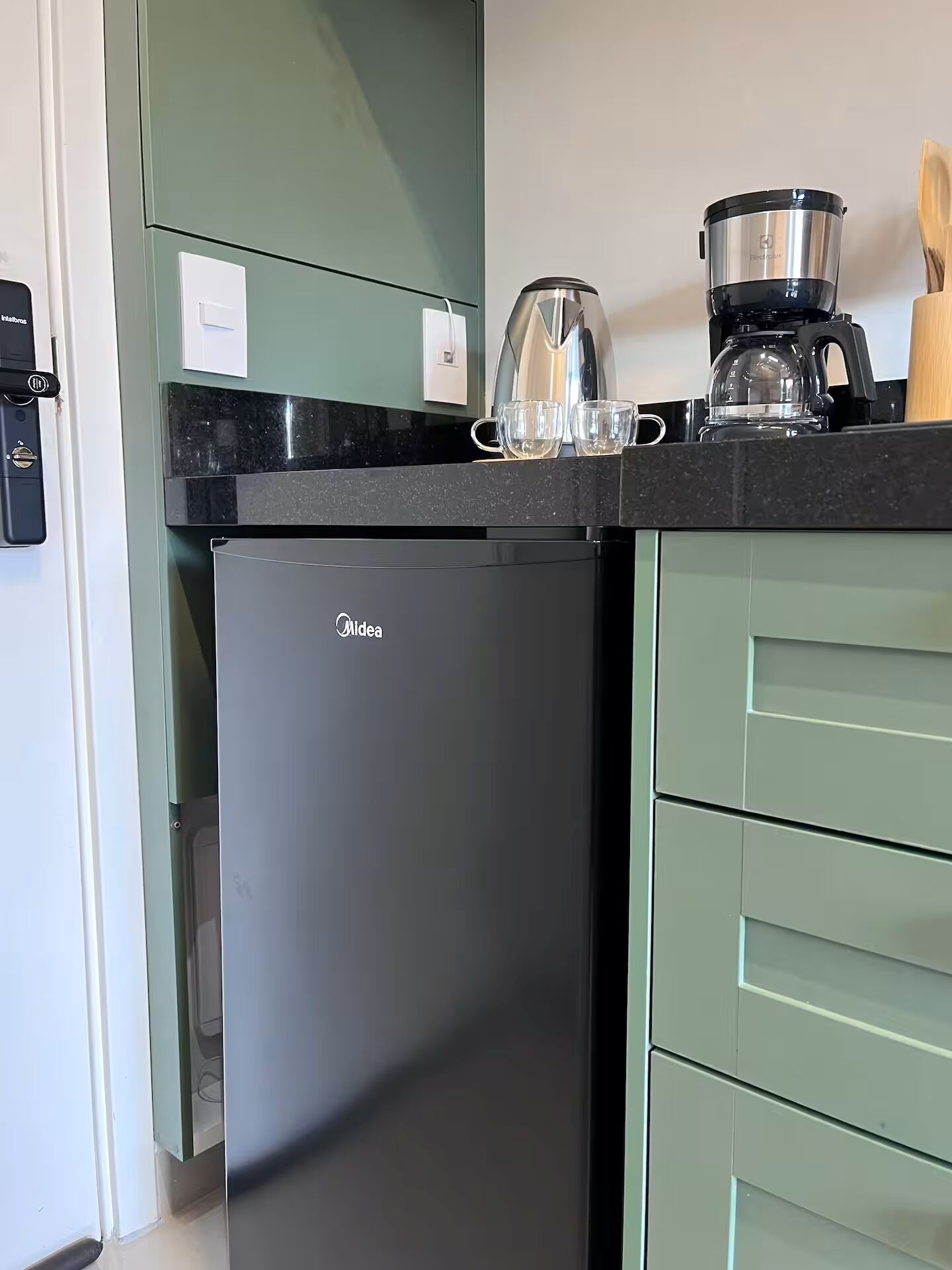 Une cuisine compacte équipée d’un réfrigérateur, d’une machine à café et d’une bouilloire posés sur le plan de travail.