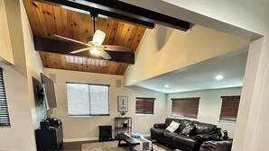 A spacious living room with a high ceiling, wooden beams, a ceiling fan, and a fireplace. - 3-bedroom cabin in amazing Running Springs with cozy vibes (Running Springs)