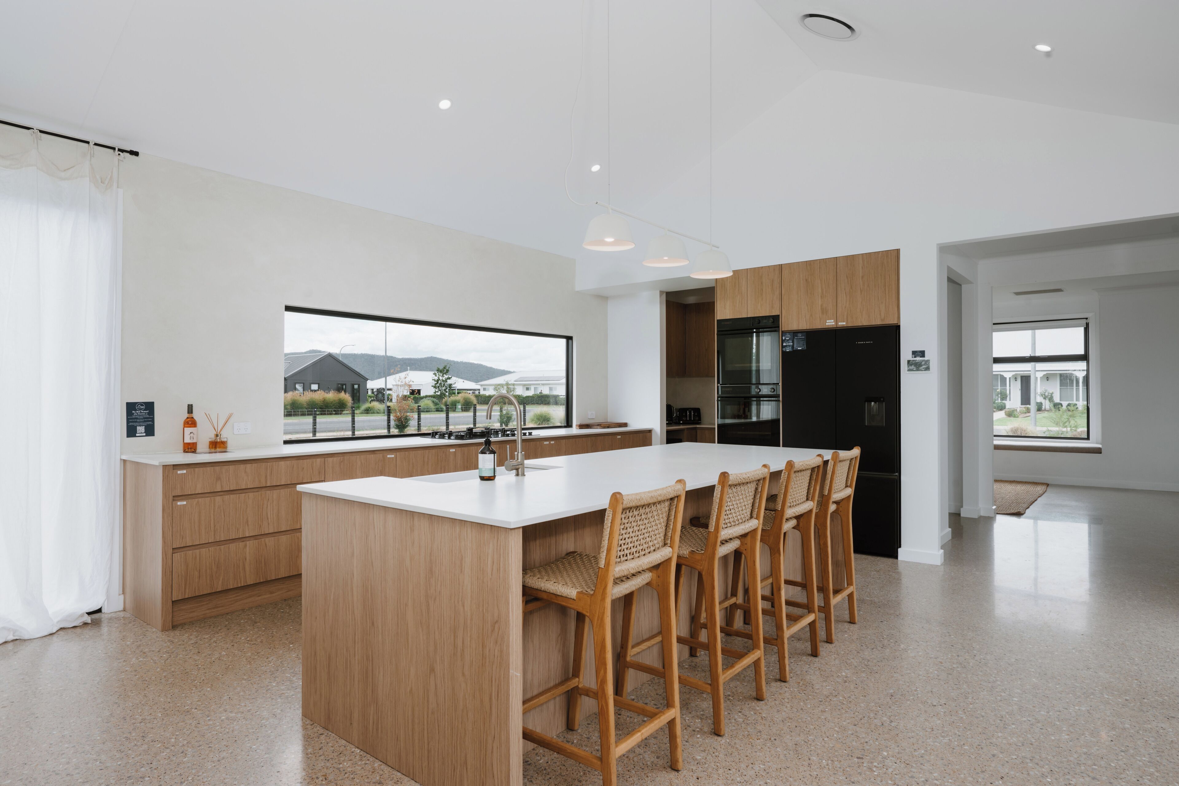 A modern kitchen with a large island, wooden bar stools, and a view of mountains through the window.