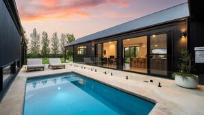 Ett modernt hus med en swimmingpool, utomhusmöbler och en matplats som är inbyggd i glas.