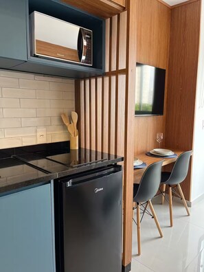 A modern kitchen with a built-in microwave, a black refrigerator, and a dining area with two chairs and a table. - Modern studio in Campo Belo, near Congonhas Airport. (São Paulo)