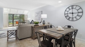 A modern living room with a dining area, a large wall clock, and a view through glass doors. - 3 Pools - PET FRIENDLY - Gulfside of Sandestin Resort (Miramar Beach)